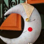 Cojín infantil con forma de luna celeste con estrellitas. La luna lleva un gorrito de dormir. El detalle perfecto para decorar el dormitorio de los niños,