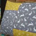 Cojín infantil en mostaza y gris, hecho a mano con telas estampadas de animales y plantas del bosque. Un cojín ideal para el dormitorio infantil.